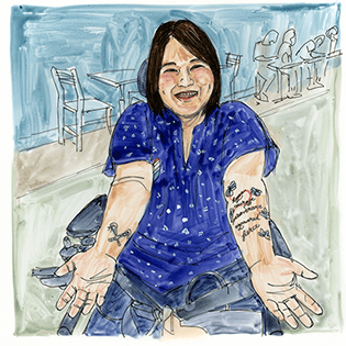 Libby sits with both arms extended, showing her tattoos. 