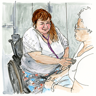 Monica sits in a wheelchair and checks a patient’s heartbeat. 